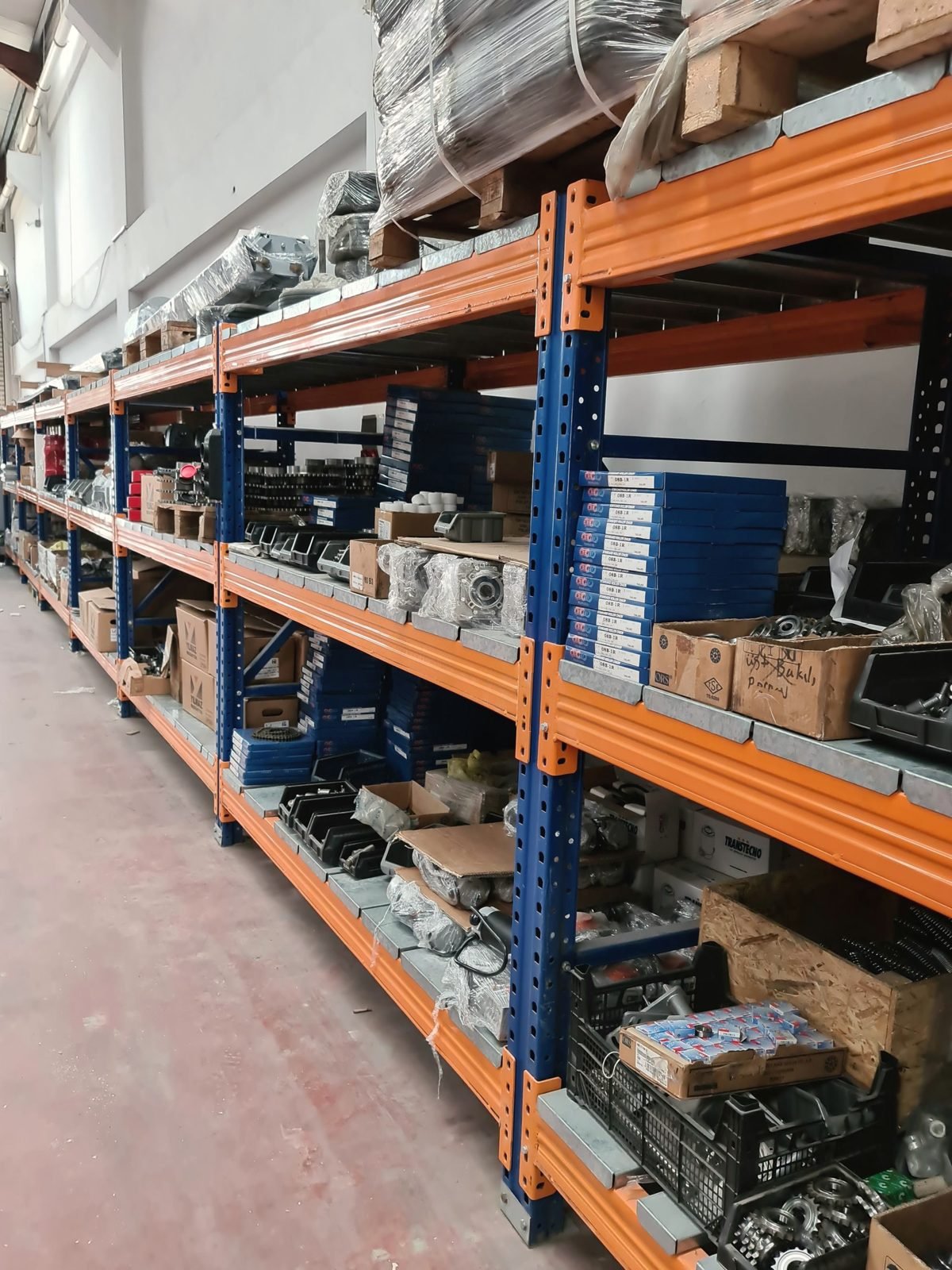A long aisle of orange and blue pallet racking stacked with boxed parts
