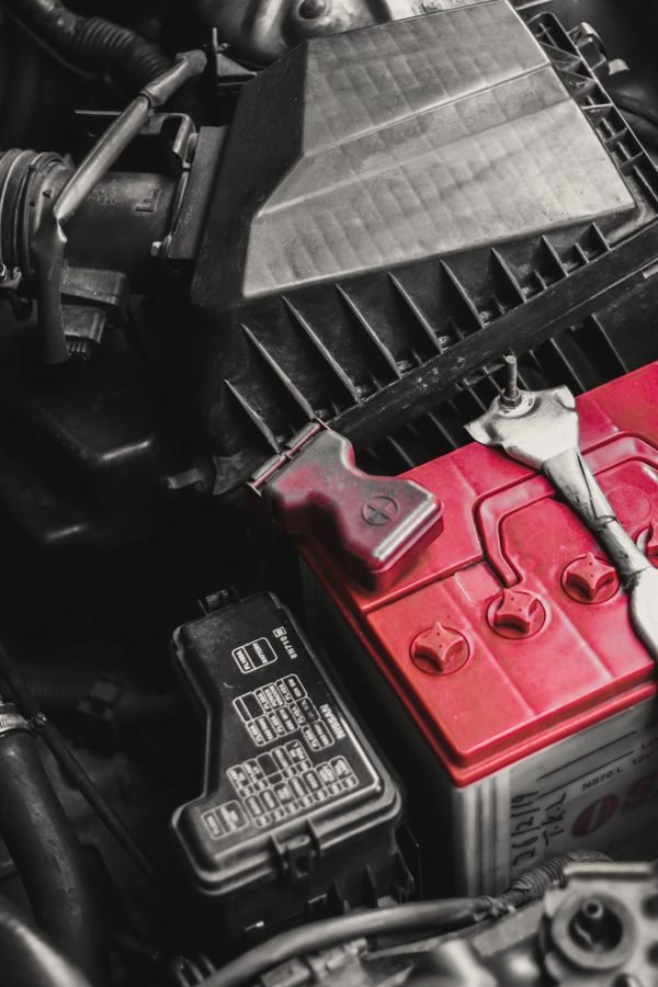 A red car battery seated in an engine bay beside the air box