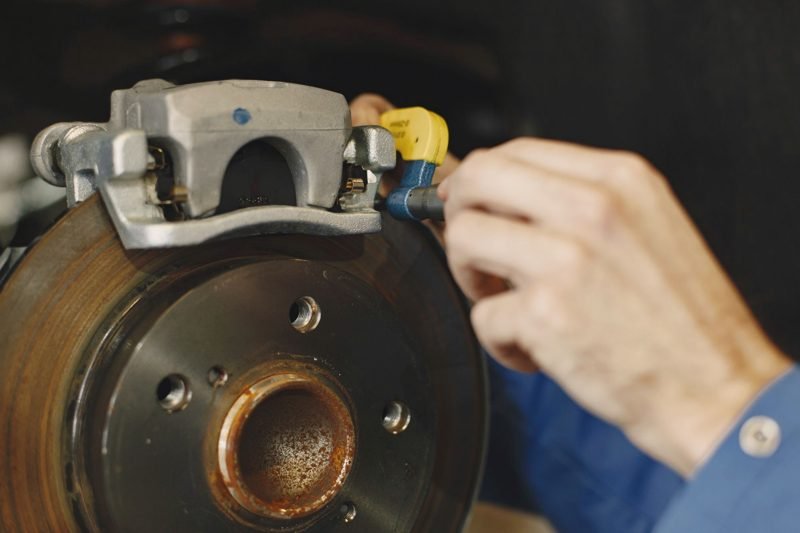A hand bleeding a brake caliper fitted over a worn rotor